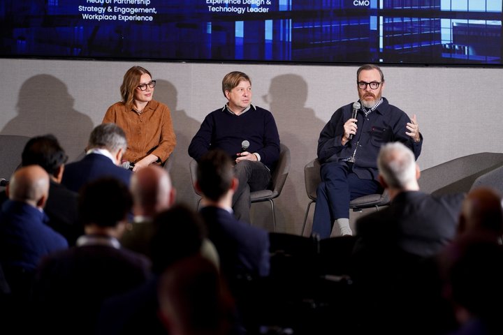 Mike McHargue seated at right, speaking into a microphone beside two fellow panelists, with audience members in the foreground.